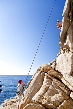 Climbers on a granitic rock on shore under blue sky, Capo Testa, Santa Teresa Gallura, Sardinia, Italy, Europe