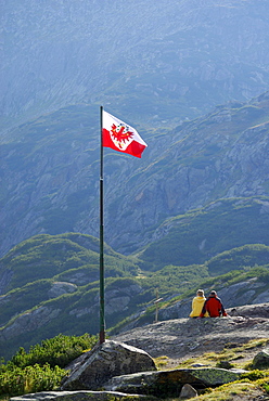 couple beneath Tyrolean flag, hut Sulzenauhuette, Stubaier Alpen range, Stubai, Tyrol, Austria