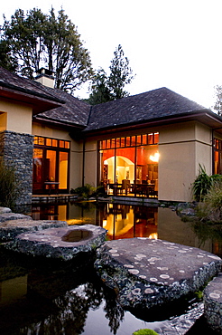 View over a pond at the illuminated windows at the Treetops Lodge in the evening, North Island, New Zealand, Oceania