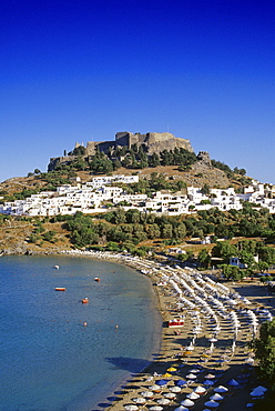 View at bay with beach, city and acropolis under blue sky, Lindos, Island of Rhodes, Greece, Europe