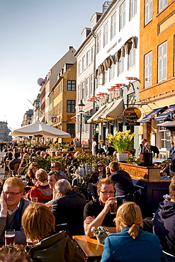 People sitting at waterfront along the Nyhavn Canal, Copenhagen, Denmark