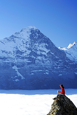 Woman sitting on rock and looking towards north face of Eiger above sea of fog, Bussalp, Grindelwald, UNESCO World Heritage Site Swiss Alps Jungfrau - Aletsch, Bernese Oberland, Bern, Switzerland, Europe