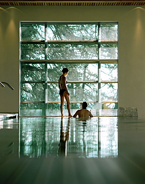 Couple at indoor pool looking out of a picture window, Vigilius Mountain Resort, Vigiljoch, Lana, Trentino-Alto Adige/Suedtirol, Italy