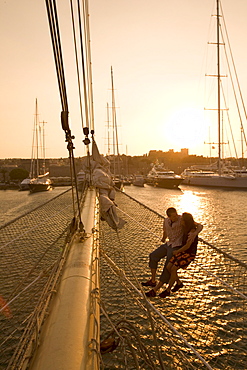 Couple in Bowsprit Net, Star Flyer, sunset over the Rhodes Harbor, Rhodes, Dodecanese Islands, Greece