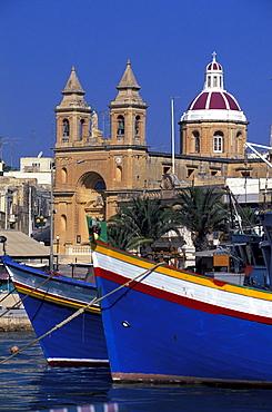 View of fishing boats at harbour and church, Marsaxlokk, Malta, Europe