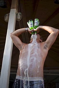 Man drinking four bottles of beer all at once during a beach party of the Super Paradise Club at Super Paradise Beach, knowing as a centrum of gays and nudism, Psarou, Mykonos, Greece