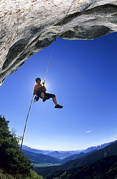 Rock climber rapelling down from an overhang of the summit of Kampenwand, view towards Tyrol, Chiemgau, Upper Bavaria, Bavaria, Germany