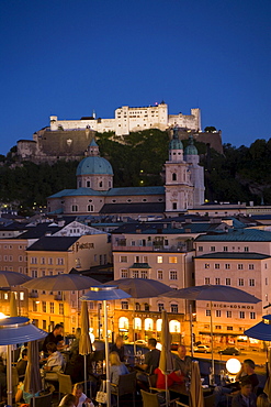 View over illuminated roof deck of restaurant Hotel Stein to old town with Salzburg Cathedral and Hohensalzburg Fortress, largest, fully-preserved fortress in central Europe, in the evening, Salzburg, Salzburg, Austria, Since 1996 historic centre of the city part of the UNESCO World Heritage Site