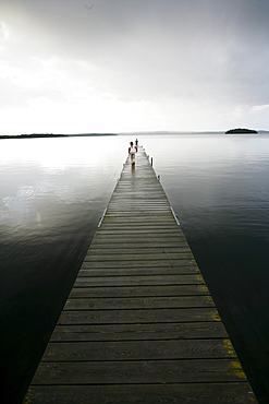 Two people standing on a wooden jetty on a cloudy day, Madkroken near Vaexjoe, Smaland, Sweden