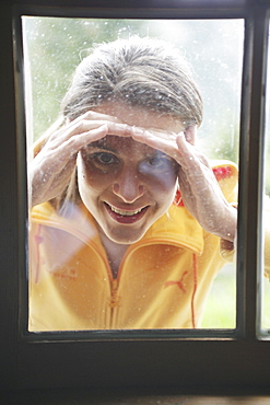 Woman looking through a window into alp lodge, Heiligenblut, Hohe Tauern National Park, Carinthia, Austria