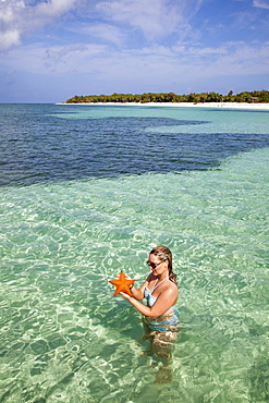 Young woman holding a red starfish in shallow water at Punta Frances Parque Nacional, Isla de la Juventud, Cuba, Caribbean