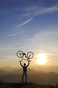 Man holding his racing bike over his head, Kraftalm, Hohe Salve, Kitzbuehel Alps, Tyrol, Austria