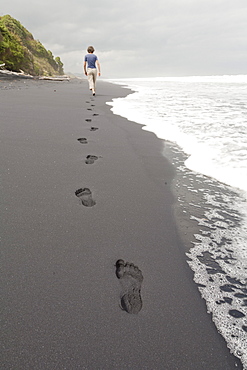 Footprints in black sand, woman walking along the beach, South Island, New Zealand