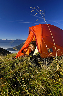 Young woman looking out of a tent in the mountains, Tyrol, Austria, Europe