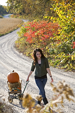 Teenage girl pulling wagon with pumpkin along path, Vittoria, Ontario