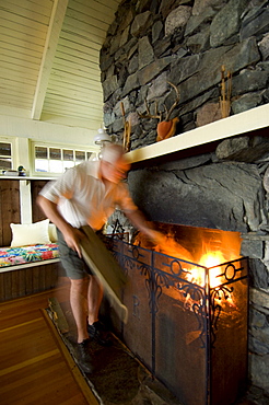 Man putting logs in cottage fireplace, Lake of the Woods, Kenora, Ontario