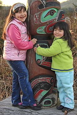 Portrait of young First Nation girls hugging a totem pole, Vancouver Island, British Columbia