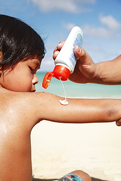 Hawaii, Oahu, Parent putting Sunscreen lotion on child's arm at the beach