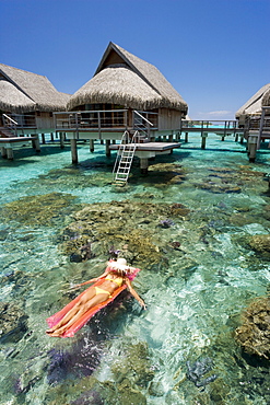 French Polynesia, Moorea, Woman sunbathing on inflatable raft over ocean reef, Luxury resort bungalows over ocean.