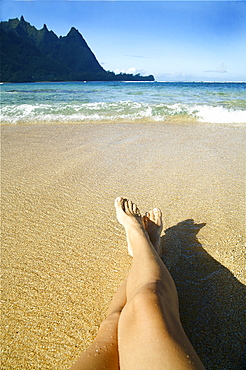 Hawaii, Kauai, Tunnels,  Womans legs relaxing on the sand.