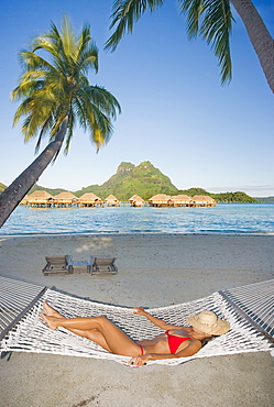 French Polynesia, Tahiti, Bora Bora, Woman resting in hammock with bungalows in the background.