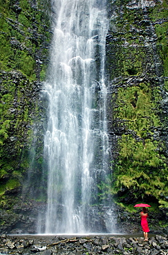 Hawaii, Maui, Kipahulu, Hana, Woman stands with umbrella at the base of waterfall.