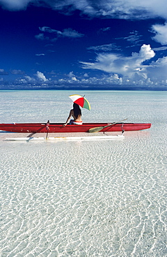 French Polynesia, Tetiaroa, Woman with umbrella in outrigger canoe floating on clear turquoise ocean, View from behind.