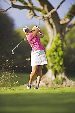 Hawaii, Maui, Wailea Gold Golf Course, Female golfer swinging golf club, turf flying from club, view from front.