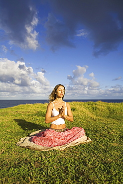 Hawaii, Maui, young woman doing yoga on grassy hill next to the ocean.