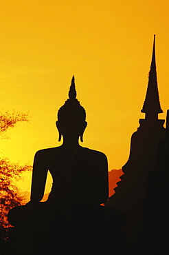 Thailand, Sukhothai, Buddha and temple silhouetted at sunset, orange sky