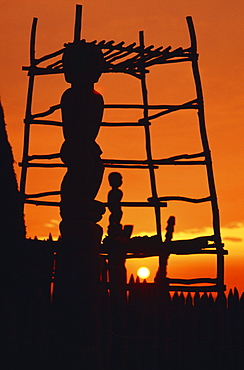 Hawaii, Big Island, Pu'uhonua O Honaunau National Historical Park, Structure and statues silhouetted by fiery sunset.