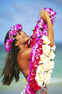 Hawaiian woman wearing haku and holding leis on beach.