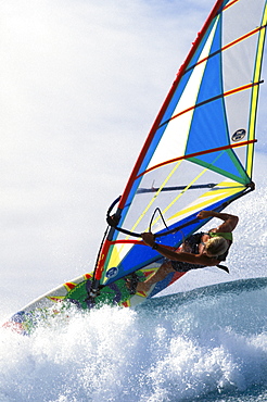 Close-up angle view of Josh Angulo over tip of wave, pale blue sky in background