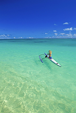 View from distance behind woman in single outrigger canoe, calm water, blue skies