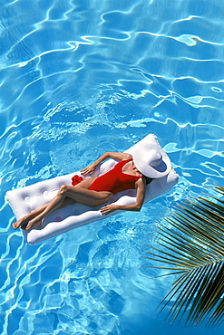 Woman floats in pool on raft, white hat 