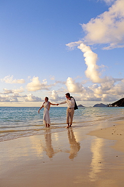 Hawaii, Romantic couple walk along shoreline at sunset