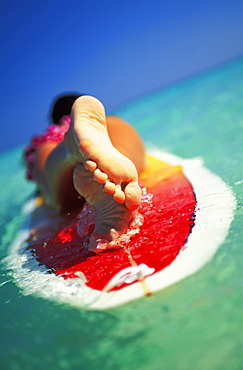 Hawaii, Oahu, Lanikai beach, close-up view from feet of woman with lei lying on surfboard