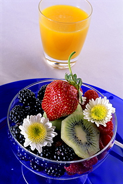 Close-up of a glass of orange juice with a bowl of fresh berries on blue dish 