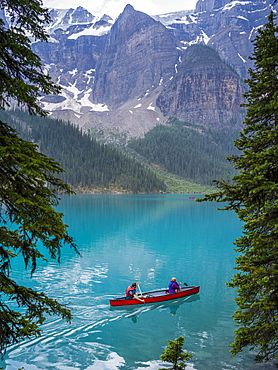 A red canoe in Moraine Lake with a cliff of the Canadian Rocky Mountains along the shoreline; Lake Louise, Alberta, Canada