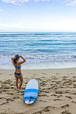 Young female surfer prepares on the beach to go out to the water, Honolulu, Oahu, Hawaii, United States of America