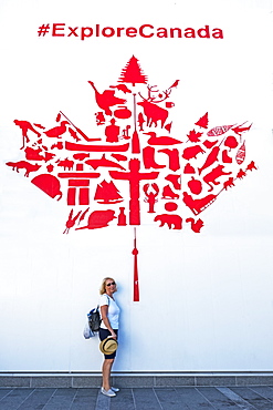 A female tourist stands under a red and white maple leaf wall mural promoting Canadian tourism, Vancouver, British Columbia, Canada