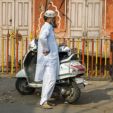 A man in traditional Indian dress stands on the street beside his motorcycle, Jaipur, Rajasthan, India