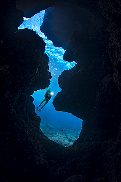 A diver (MR) shines her light into a crevice opening off Kaiwe Point on the Kona coast, Island of Hawaii, Hawaii, United States of America