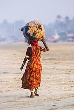 Karnataka woman walking on the beach carrying a bundle on her head, Goa, India