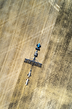 Aerial view of air seeder in field with white ammonia tanks, near Beiseker, Alberta, Canada