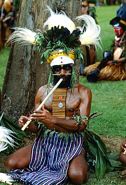 Bearded tribesman wearing feathered headdress and playing a pipe during  a gathering of tribes at Mount Hagen in Papua New Guinea