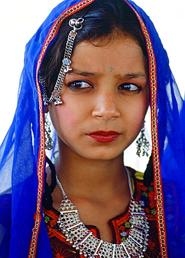 A young girl in traditional costume with silver filigree necklace and earrings and a brightly coloured veil, Pakistan