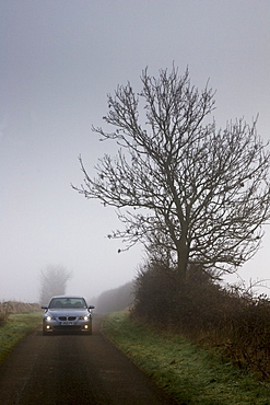 BMW 5-series car drives along empty country road in adverse foggy weather, Oxfordshire,  England, United Kingdom