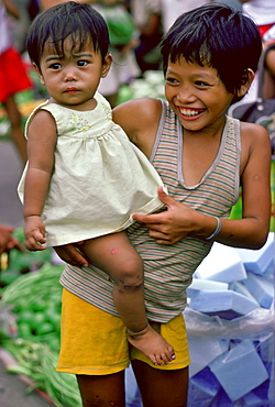 A young boy carrying his sister through the  Manila markets in the Philippines