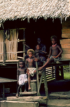 Mother and children at their traditional wood and straw roofed home in the Solomon Isles.